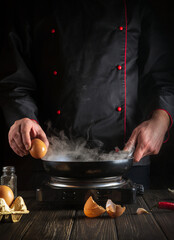 Professional chef tries to break an egg on a frying pan to make delicious breakfast. Working environment in the kitchen. Menu idea for a restaurant or hotel