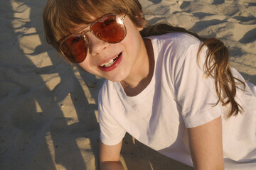 A girl is sitting on a wooden chaise longue on the beach in pink glasses . Reflection in glasses