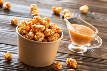 Caramelized popcorn in paper bucket on wooden table