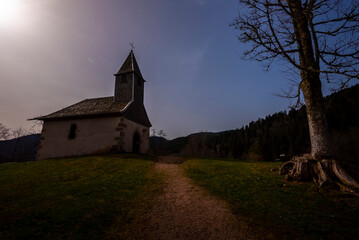 Fototapeta premium Nuit américaine sur une petite chapelle européenne en haut d'une colline au milieu des montagnes de sapin.