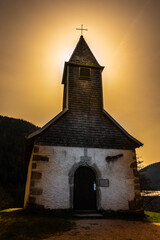 Petite chapelle médiévale au bord du lac de Longemer dans les Vosges photographier à contre jour sous un ciel étrange et fantastique