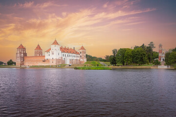 Mir Castle landmark on river against backdrop of sunset sky