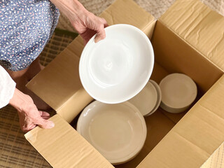 ダンボール箱に食器を入れる高齢女性の手