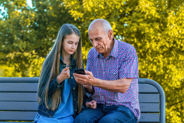 Senior grandfather learning to using smart phone under guidance of pretty granddaughter sitting on...