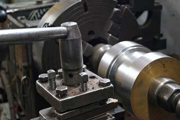 Closeup of a metal shaft parts cutting by old Lathe Machinery. lathe chuck and key 4-jaw screw chuck. Vintage Industrial Machinery in a old factory. Selective focus.