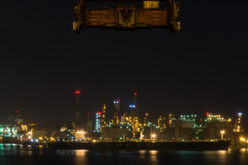 Fototapeta na wymiar view of industrial port in night with chimney, oil tanks, pipes and crane