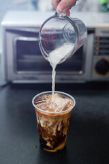 Ice coffee on a plastic cup with cream being poured into it showing the texture