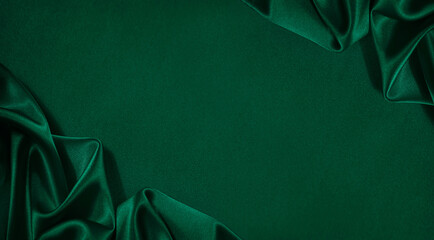 Dark green silk satin background. Wavy folds. Smooth surface. Shiny fabric. Luxury background with copy space for design. Web banner. Top view table. Flat lay. Wide.