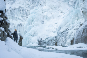 Hiker overlooking frozen waterfalls from their bottom on a cold winter day, Yoho N. Park, Canada