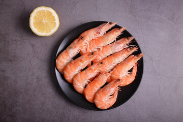 Portion of cooked prawns on a dark gray table and garnished with lemon