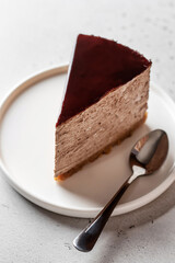 Chocolate cheesecake slice on a white plate with a spoon on white background
