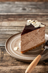 Chocolate cheesecake slice with almond petals topping on ceramic plate with fork on wooden background. Copy space