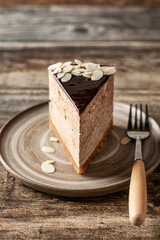 Chocolate cheesecake slice with almond petals topping on ceramic plate with fork on wooden background