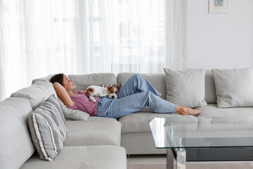 Portrait of young beautiful woman lying on the couch with her adorable wire haired Jack Russel...