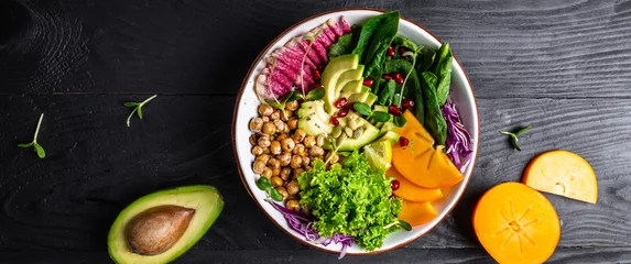 Zelfklevend Fotobehang Fresh salad with roasted chickpeas, avocado, persimmon, spinach, avocado, watermelon radish and seeds on a dark background. Long banner format. top view © Надія Коваль