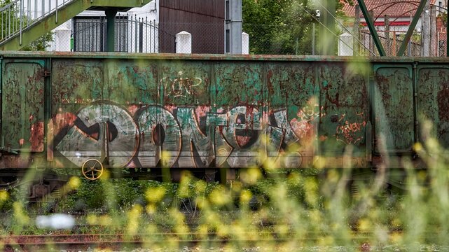 Monforte de Lemos, Spain; 05-21-2022: Old abandoned train freight car on the tracks of the train station of a town rusty and painted with graffiti among vegetation