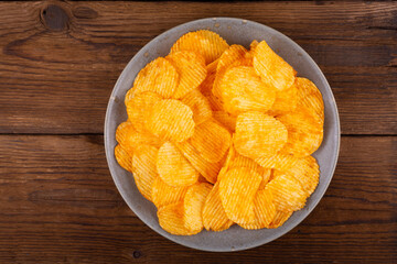 Potato wavy chips in bowl on wooden background, top view.