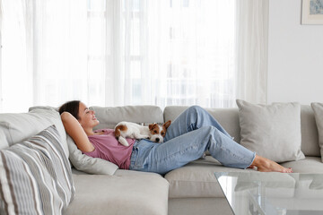 Portrait of young beautiful woman lying on the couch with her adorable wire haired Jack Russel...