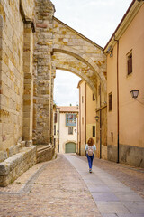 Fototapeta na wymiar Woman strolling through the old medieval city with stone arches, Zamora Spain.