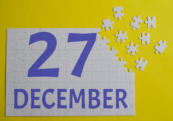27 december calendar date on a white puzzle with separate details. Puzzle on a yellow background with a blue inscription