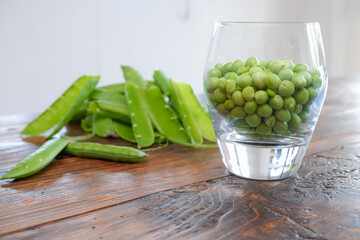 Green peas in glass bowl. fresh pea in the pod with green leaves. green peas on a brown wodden table