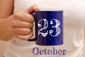 The inscription on the blue cup 23 october. Cup in female hand, business concept