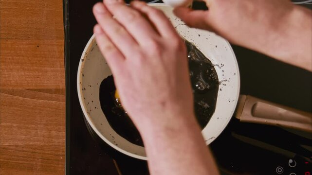 male hands break an egg into a frying pan in black oil. fried eggs in black oil, similar to unfiltered petroleum products. boiling dark oil frame from above 100fps 2.8k top shot