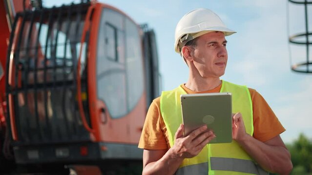 worker in hard a hat with digital tablet near excavator. construction site driver with online digital tablet. industry business construction concept. worker hard hat near excavator truck in uniform.