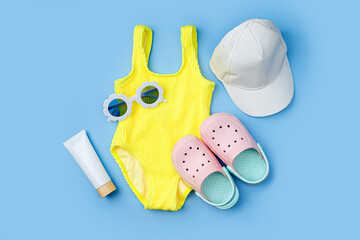 Bright yellow swimsuit, sunglasses, beach slippers and sunscreen for children on blue background....