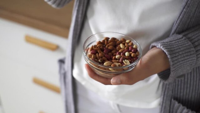 Girl woman holding peanuts in a transparent bowl, breakfast in the kitchen girl holding peanut nuts in her hands, proper nutrition breakfast high-calorie food
