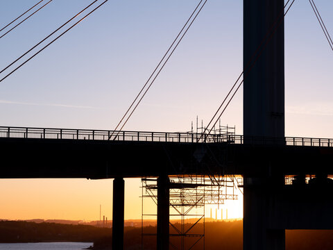 Silhouette of suspension bridge and scaffolding for repair work. Shot into rising sun