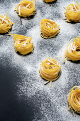 Homemade raw twisted pasta with flour on black table. Mediterranean food background.