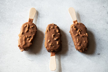 Chocolate almond ice-cream on a wooden stick on a gray background. Top view.