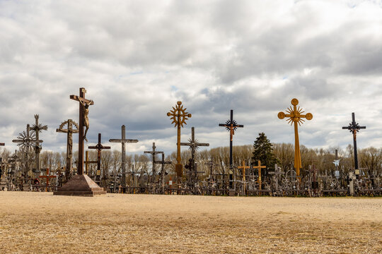 Low angle view to different design crosses at hill of crosses near Šiauliai, Lithuania. Handmade artsy catholic crosses in different sizes at cloudy day. Pilgrimage site for Christians at early spring