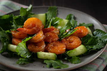 Fresh salad with grilled shrimps, cucumbers and arugula beautifully served on a plate