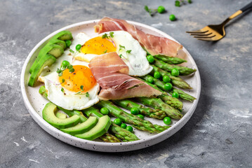 Tasty breakfast. avocado, asparagus, jamon, ham, prosciutto and fried egg on white plate. banner, menu recipe place for text, top view