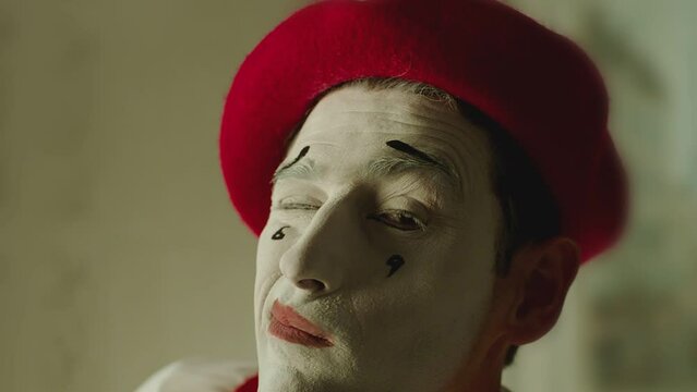 Close up portrait of french pantomime artist making different emotions and gestures of smile ,  closing one eye , sending air kiss, giving rose . White color makeup with tears .  Shot on ARRI camera  