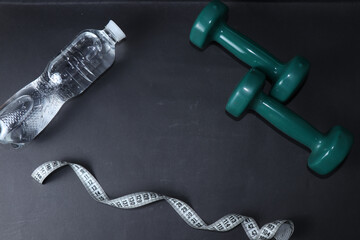 Dumbbells, a bottle of water and a centimeter tape isolated on a black background. Sports Weight Loss Kit