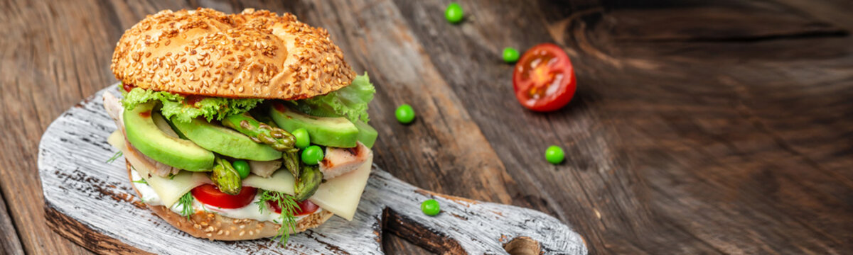 Homemade burger with grilled chicken fillet, asparagus, avocado, tomatoes, peas, cheese and tartar sauce on rustic wooden background. fast food and junk food concept