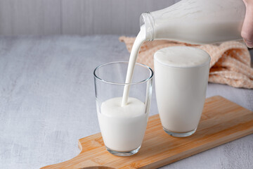 Pouring homemade kefir, buttermilk or yogurt with probiotics. Yogurt flowing from glass bottle on...