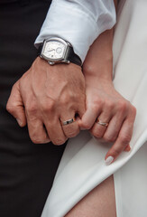 close up male and female hands with wedding rings. happy newlyweds arms. bride is holding hand groom with fingers on white dress and black pants background. wedding details concept, free space