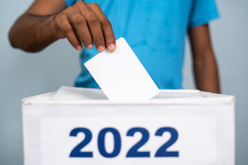 Man placing ballot paper into 2022 ballot box - concept of 2022 election. voting and democracy