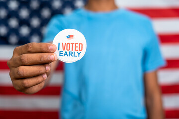 close up shot of young man showing I voted early stick in front of US american flag - concept of early voting or polling.