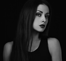 Fototapeta premium Beautiful bright makeup woman with red lipstick in black top and long brown healthy hair looking on dark black shadow background. Closeup