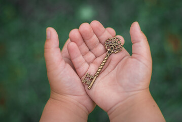 Forged old key from the door close-up on the palms of a child. Brass carved vintage key on a green background.
