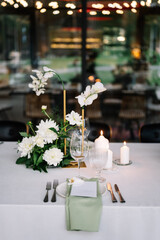 table setting for a wedding, white dishes on a wedding table with elements of green leaves and white flowers, themed decor. Menu card