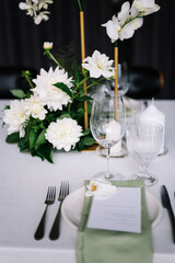 table setting for a wedding, white dishes on a wedding table with elements of green leaves and white flowers, themed decor. Menu card