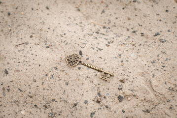 A handmade bronze door key lies in the sand.
Lost carved ancient key close-up.