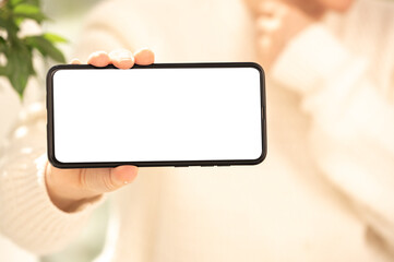 Cell phone mockup. woman in white clothes shows blank white cell phone screen in horizontal position. Mobile phone with white screen in female hand.