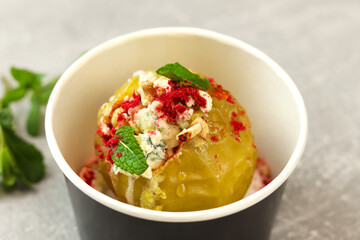 Baked apple with blue cheese, spices and nuts in a takeaway box  on a gray background. Healthy food delivery concept.